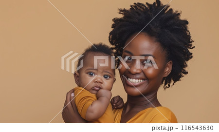 a smiling African woman holding a three-month-old baby, both wearing matching yellow outfits  116543630