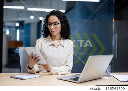 A professional woman in an office environment wearing glasses, focused and utilizing a tablet alongside laptop, symbolizing productivity and technology use in the modern workplace A professional woman in an office environment wearing glasses, focused and utilizing a tablet alongside laptop, symbolizing productivity and technology use in the modern workplace 116543700