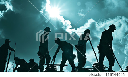 A silhouette of construction workers against a bright, cloud-filled sky 116544043