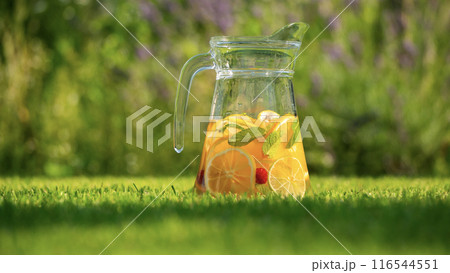 Pitcher of citrus-infused lemonade on the green grass in the backyard Pitcher of citrus-infused lemonade on the green grass in the backyard 116544551