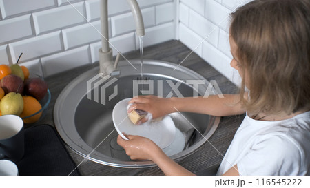 Focused young girl in a white t-shirt washing dishes in the kitchen sink 116545222