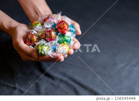 Vienna, Austria August 20, 2022. Beautiful image with a group of Lindt Lindor chocolates, of different shapes, in multicolored wrappers held by two hands. Copy space. 116545449