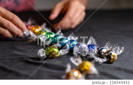 Vienna, Austria August 20, 2022. Beautiful image with group of Lindt Lindor chocolates, different shapes in multicolored wrappers. A hand in the background grabs one. Concept of relaxation, pampering. 116545452