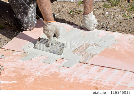 Applying cement-based adhesive mortar to thin flexible panel of fake brickwork to finish facade of house. 116546032