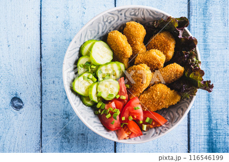 Close up of bowl with crispy nuggets, tomato and cucumber on the table top view 116546199