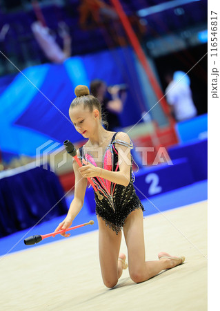 A young rhythmic gymnast shows agility and artistry performing with clubs on a competitive stage 116546817