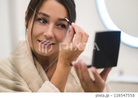 Pretty young woman looking in the mirror and making her eyebrows Pretty young woman looking in the mirror and making her eyebrows 116547558