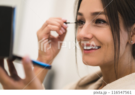 Cute dark-haired young woman doing her make up and looking contented Cute dark-haired young woman doing her make up and looking contented 116547561