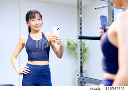 スポーツジムでスマホで腹筋を撮影する若い女性　パーソナルジム　筋トレ女子　個室　自撮り　セルフィー 116547593