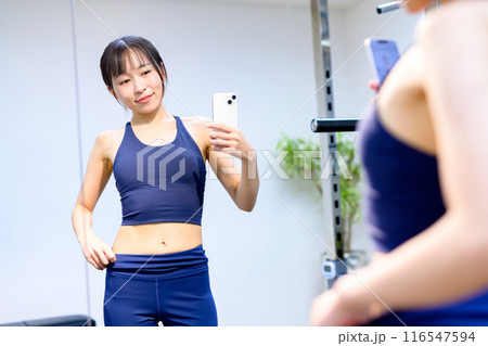 スポーツジムでスマホで腹筋を撮影する若い女性　パーソナルジム　筋トレ女子　個室　自撮り　セルフィー 116547594