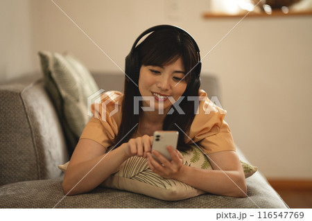 ソファに寝転んでスマホ音楽を聴くミドルの女性 ソファに寝転んでスマホ音楽を聴くミドルの女性 116547769