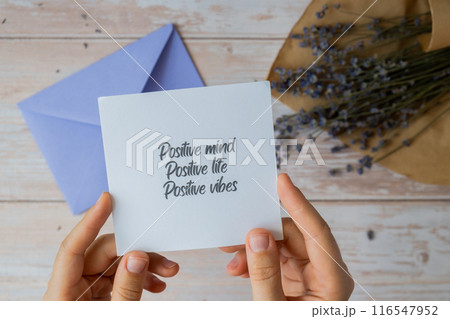 Female hands taking paper card note with text POSITIVE MIND LIFE VIBES from violet envelope. Lavender flower. Top view, flat lay. Concept of mental spiritual health self care wellbeing Female hands taking paper card note with text POSITIVE MIND LIFE VIBES from violet envelope. Lavender flower. Top view, flat lay. Concept of mental spiritual health self care wellbeing 116547952