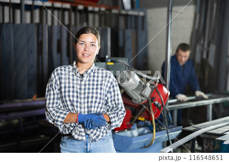 Smiling female worker standing in front of profile cutting machine Smiling female worker standing in front of profile cutting machine 116548651