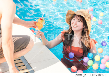 バカンスに来てプールサイドの男性からトロピカルドリンクをもらうプールの中の水着の女性 バカンスに来てプールサイドの男性からトロピカルドリンクをもらうプールの中の水着の女性 116548922