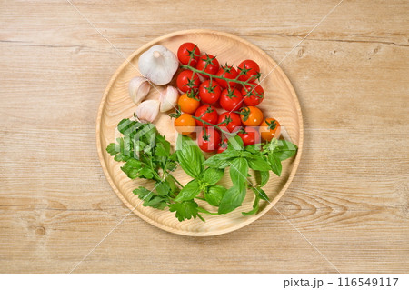 イタリアン料理用のハーブと野菜の食材イメージ。ミニトマト、イタリアンパセリ、バジル、にんにく。 イタリアン料理用のハーブと野菜の食材イメージ。ミニトマト、イタリアンパセリ、バジル、にんにく。 116549117
