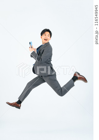 スマホを持ってジャンプする男性ビジネスパーソンの全身写真 スマホを持ってジャンプする男性ビジネスパーソンの全身写真 116549945