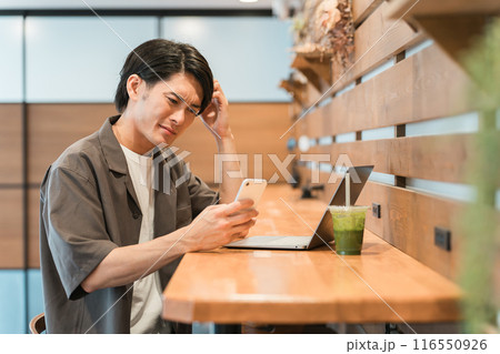 スマホを見てショックを受ける若いアジア人男性（炎上・失敗・ミス・困る・悩む・後悔・自己嫌悪） 116550926