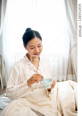 A beautiful young Asian woman in pajamas is mixing her facial treatment mask on her bed. 116551454