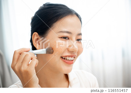 A beautiful Asian woman is applying a facial treatment mask to her face with a brush. 116551457