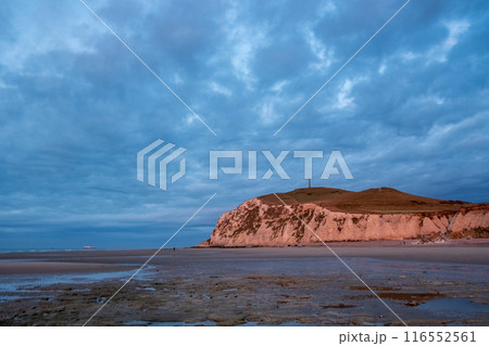 Enjoy a captivating view of a dramatic coastal sunset over a rocky cliff with a cloudy sky 116552561