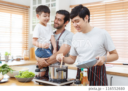 Happy cheerful LGBTQ couple cooking a food together in kitchen, a LGBT couple with adopted child cooking a food. Diversity lifestyles concept. 116552680