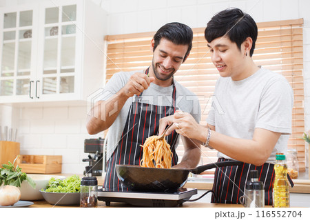 LGBTQ+ gay bisexual cooking their meal together in the kitchen, LGBTQ gay couple making a spaghetti. A different ethnicity handsome gay couple enjoy cooking a spaghetti together in kitchen. 116552704