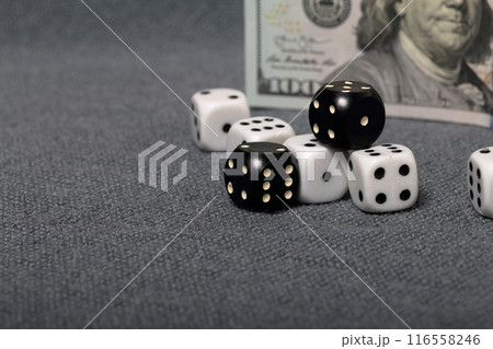 White dice with black markings. They lie on a surface covered with a coarse gray cloth. Among them are two black dice with white markings. Nearby is a hundred dollar bill. White dice with black markings. They lie on a surface covered with a coarse gray cloth. Among them are two black dice with white markings. Nearby is a hundred dollar bill. 116558246