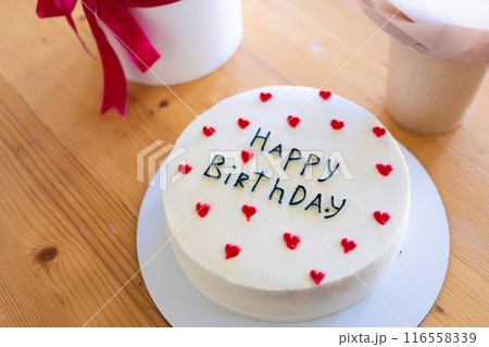 Birthday cake with the words Happy Birthday written on it, surrounded by red heart decorations. 116558339