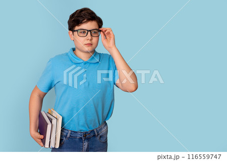 A cute teenage boy in glasses and a blue T-shirt, holding a stack of books A cute teenage boy in glasses and a blue T-shirt, holding a stack of books 116559747