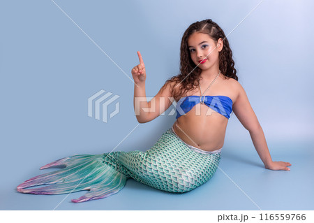 A smiling child girl in a mermaid costume sits on a blue background 116559766