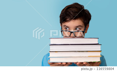 A teenage boy with glasses peeks out from behind a stack of books 116559804