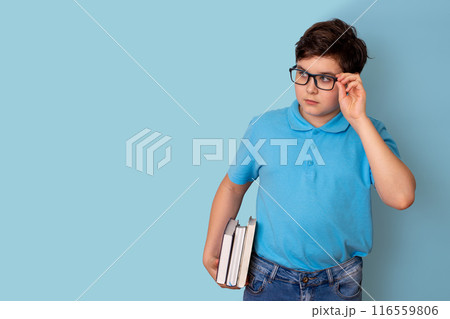 A teenage boy in glasses and a blue T-shirt, holding a stack of books 116559806