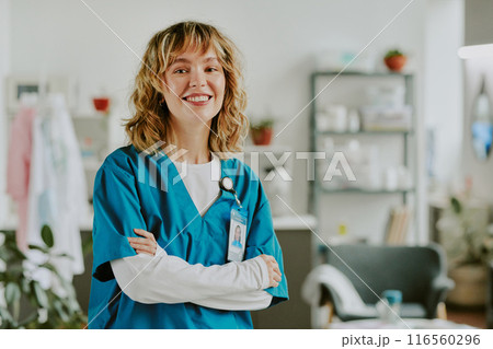 Golden haired Caucasian nurse smiling widely and crossing her arms while sitting for portrait in on call room Golden haired Caucasian nurse smiling widely and crossing her arms while sitting for portrait in on call room 116560296