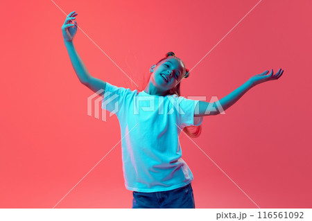 Portrait of young girl in white t-shirt and jeans spreading hands in positive expression against pink background in neon light 116561092