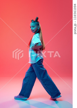 Full-length image of young girl in casual clothes, white t-shirt and jeans, with stylish hairstyle, dancing modern dance style against pink background in neon light Full-length image of young girl in casual clothes, white t-shirt and jeans, with stylish hairstyle, dancing modern dance style against pink background in neon light 116561094