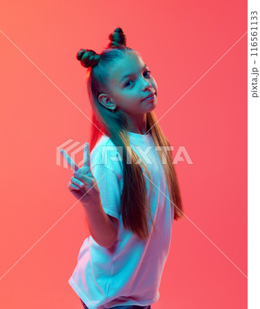 Portrait of pretty young girl in white t-shirt and stylish hairstyle, posing, showing peace gesture with hands against pink background in neon light 116561133