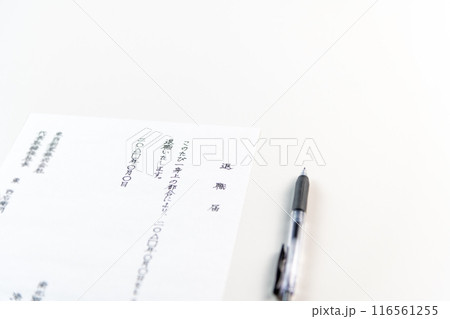 白いテーブルに置かれた手書きの退職届とゲルインクの黒ペン 116561255