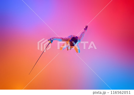 Fencer in uniform and mask in impressive jump, holding rapier forward in mixed neon lights against gradient studio background. Fencer in uniform and mask in impressive jump, holding rapier forward in mixed neon lights against gradient studio background. 116562051