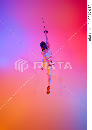 Top-down view of fencer in action, lunging with his epee performing his power and strength during battle in mixed neon lights against gradient studio background. Top-down view of fencer in action, lunging with his epee performing his power and strength during battle in mixed neon lights against gradient studio background. 116562055