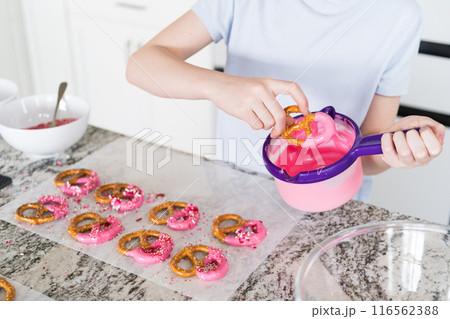 Freshly dipped and still glistening, these crunchy pretzels are lovingly adorned with pink chocolate and a scattering of colorful sprinkles, promising a feast for the senses. 116562388