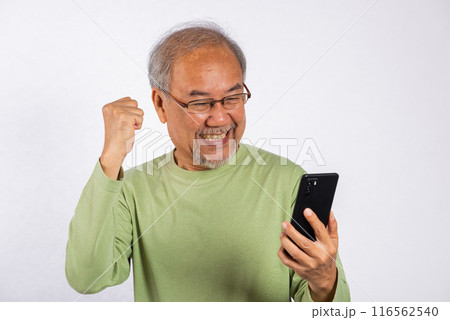 Portrait Asian smiling old man holding a cell phone celebrating something on the phone studio shot isolated on white background, happy senior man doing winner gesture celebrate on mobile phone Portrait Asian smiling old man holding a cell phone celebrating something on the phone studio shot isolated on white background, happy senior man doing winner gesture celebrate on mobile phone 116562540