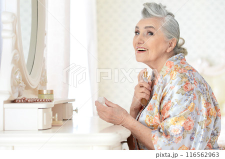 Smiling senior woman doing makeup in front of mirror at home 116562963
