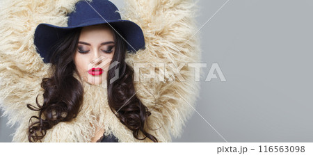 Charming young brunette lady with makeup and long curly hair posing on blue background 116563098