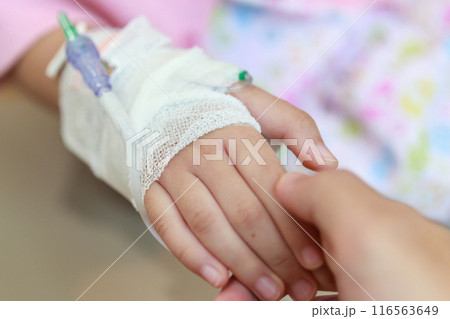 Mother holding child hand with saline IV solution in hospital 116563649