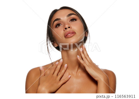 Portrait of beautiful young woman with black hair in ponytail, tanned well-kept skin and glowing body, touching neck isolated on white background 116563911