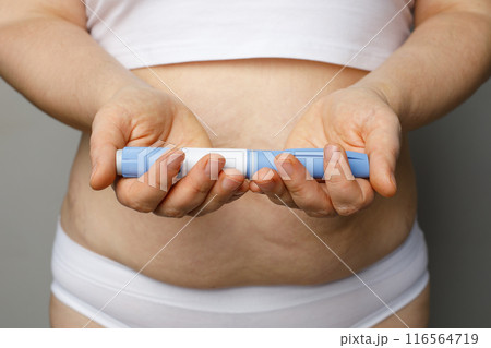 Injection pen in female hands indoor. Semaglutide or insulin drug against female belly. Semaglutide 116564719