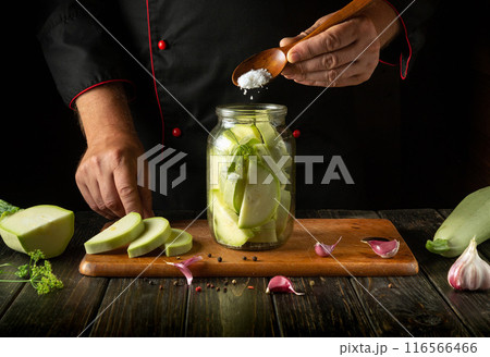 Chef spoons salt into a jar of chopped vegetable marrow before canning it with spices. Concept of pickling delicious zucchini on a restaurant kitchen table Chef spoons salt into a jar of chopped vegetable marrow before canning it with spices. Concept of pickling delicious zucchini on a restaurant kitchen table 116566466