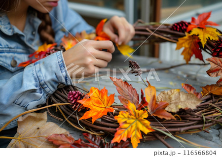 Girl making a wreath with autumn leaves and pine cones 116566804