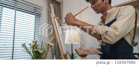 Young Artist Painting on Canvas in Modern Home Studio with Natural Light and Flowers 116567060