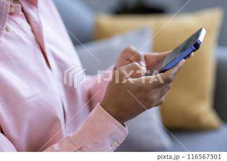 Person using smartphone at home on sofa. Casual attire adds relaxed feel to image that emphasizes connection, technology, and communication. Ideal for representing concepts like home life 116567301